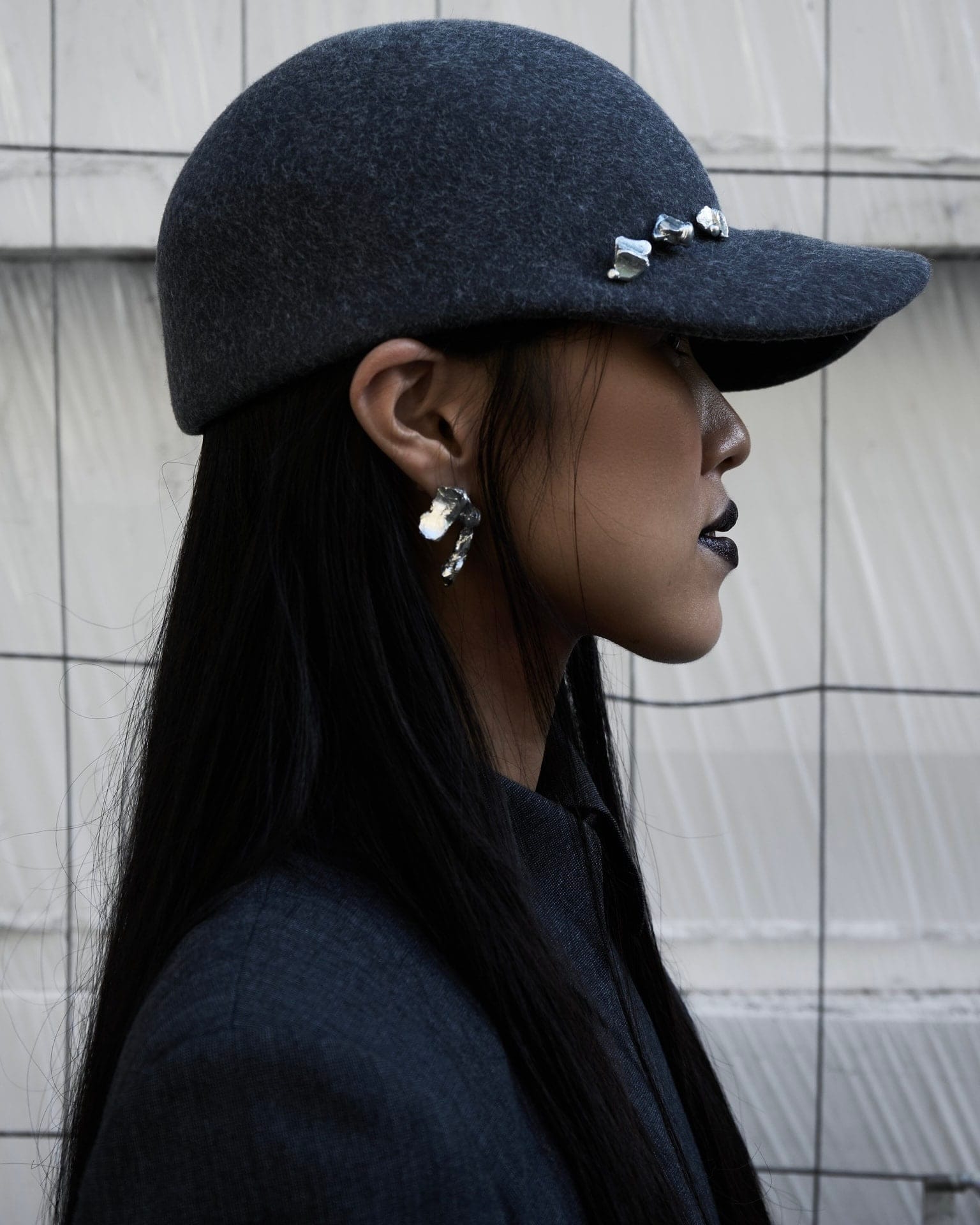 profile of a person in a dark felt cap studded with silver, a silver earring below