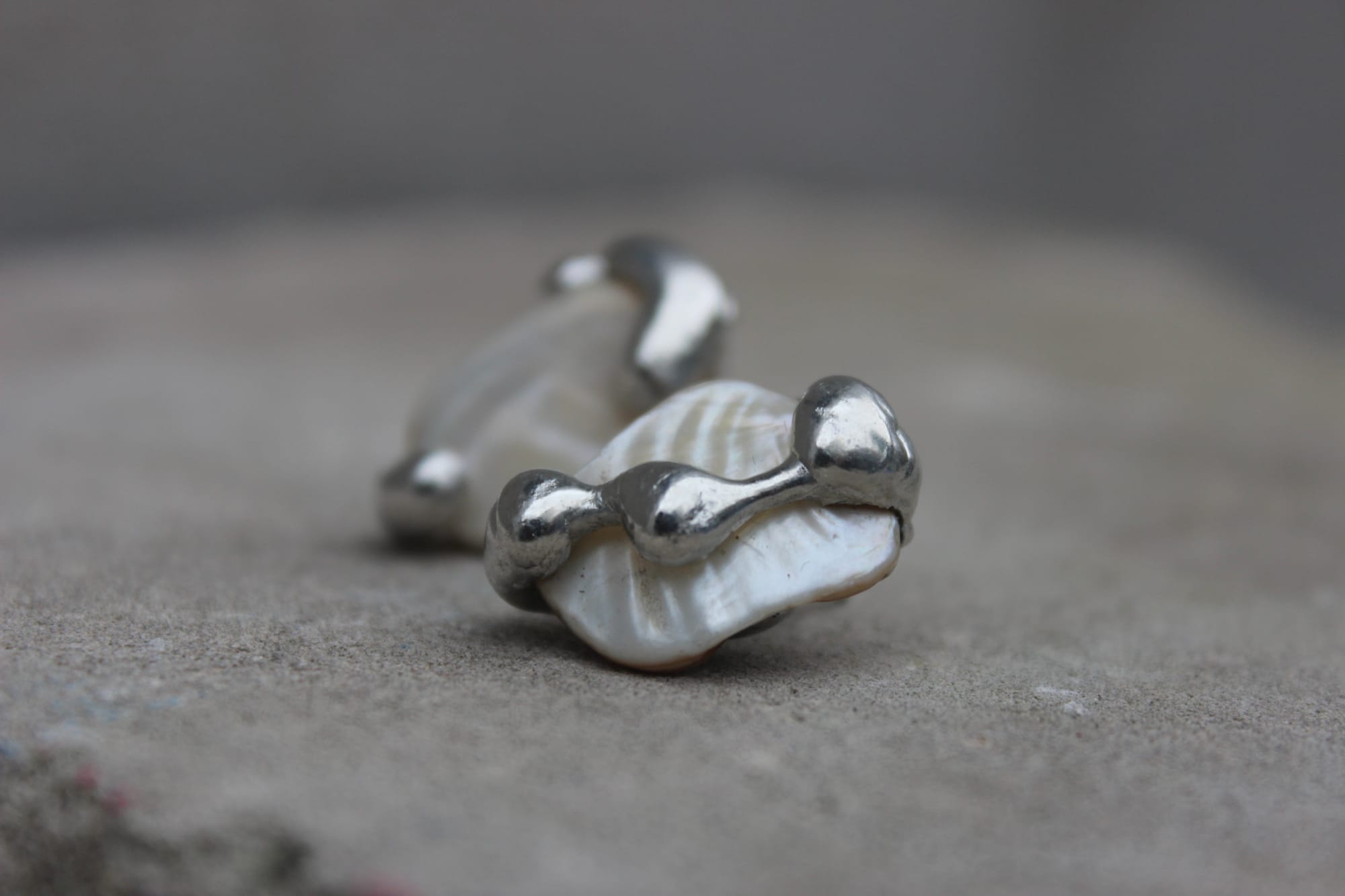 two mother-of-pearl pieces held in silver, resting on concrete