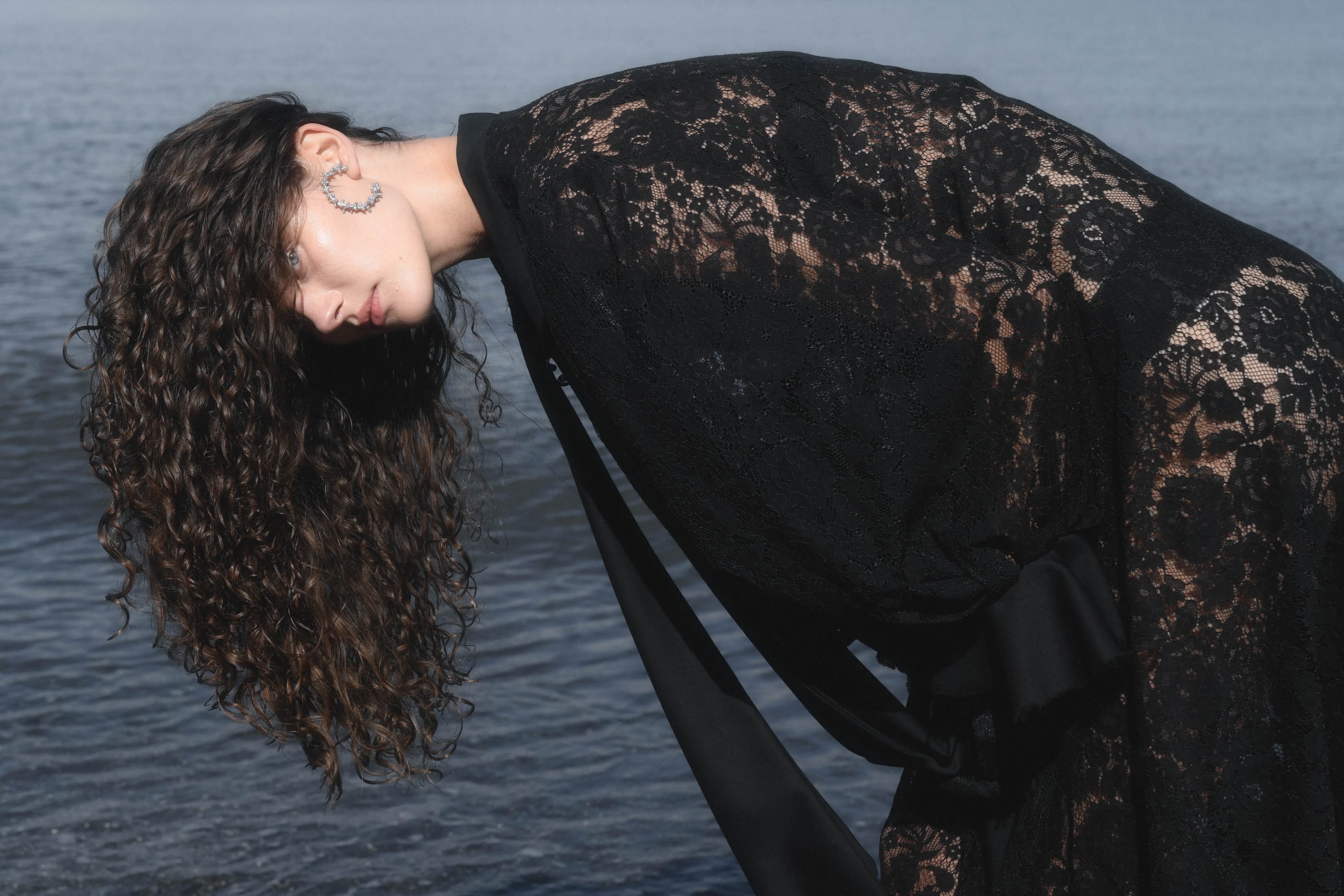 a person in black lace bending forward over a grey sea