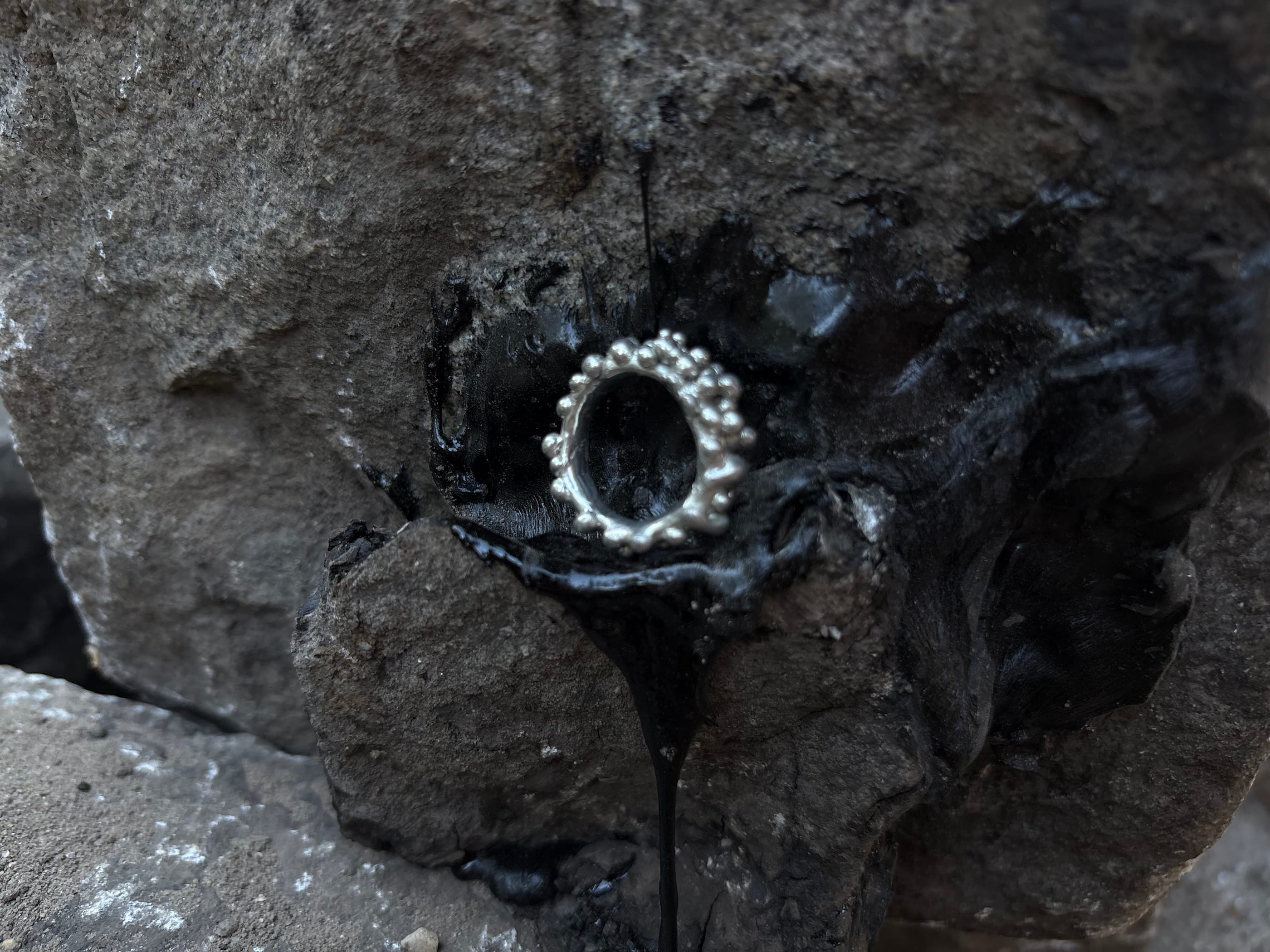 a beaded silver ring set into dark volcanic rock, black resin running beneath it