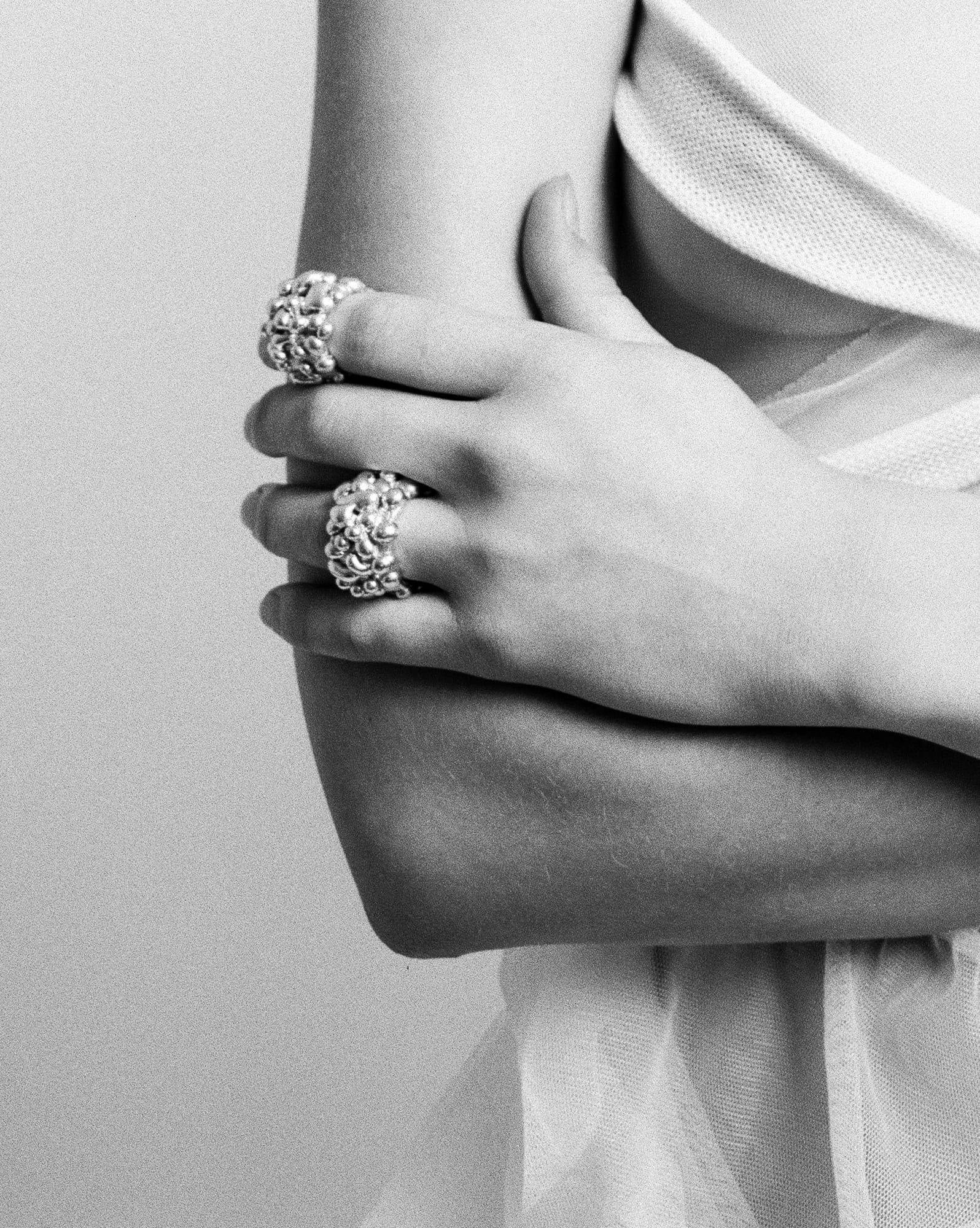 crossed arms wearing two textured silver rings, in black and white