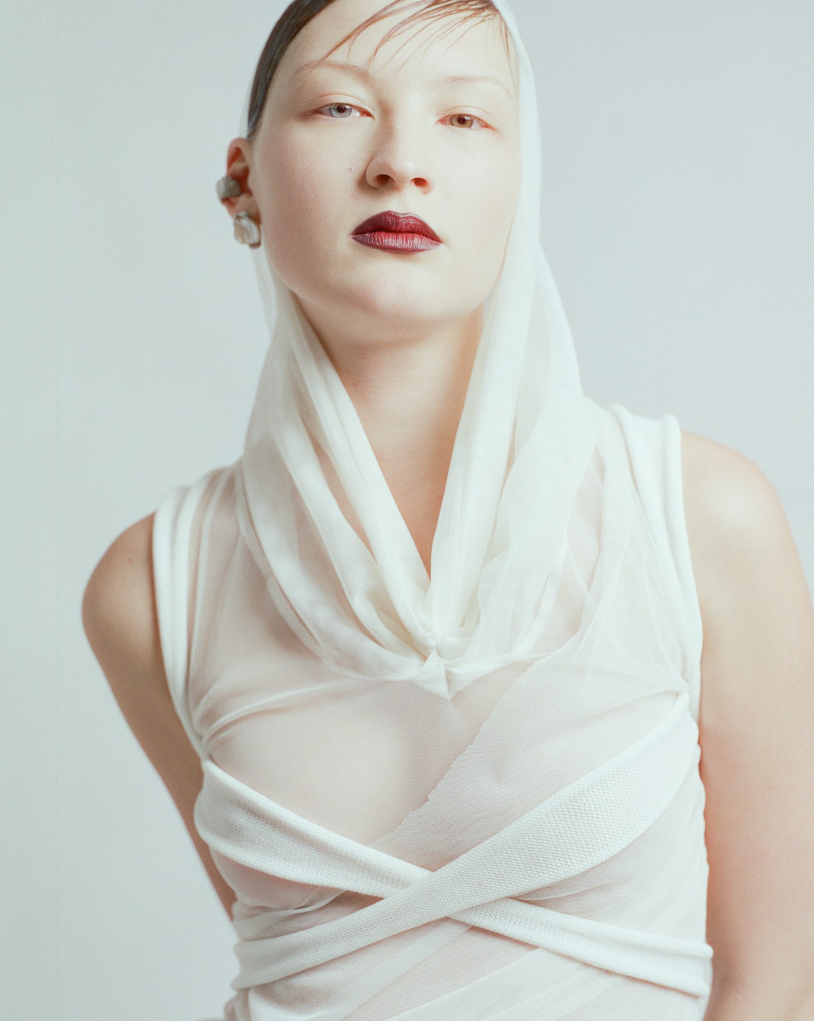 portrait of a person in a white draped top and hood, silver at the ear