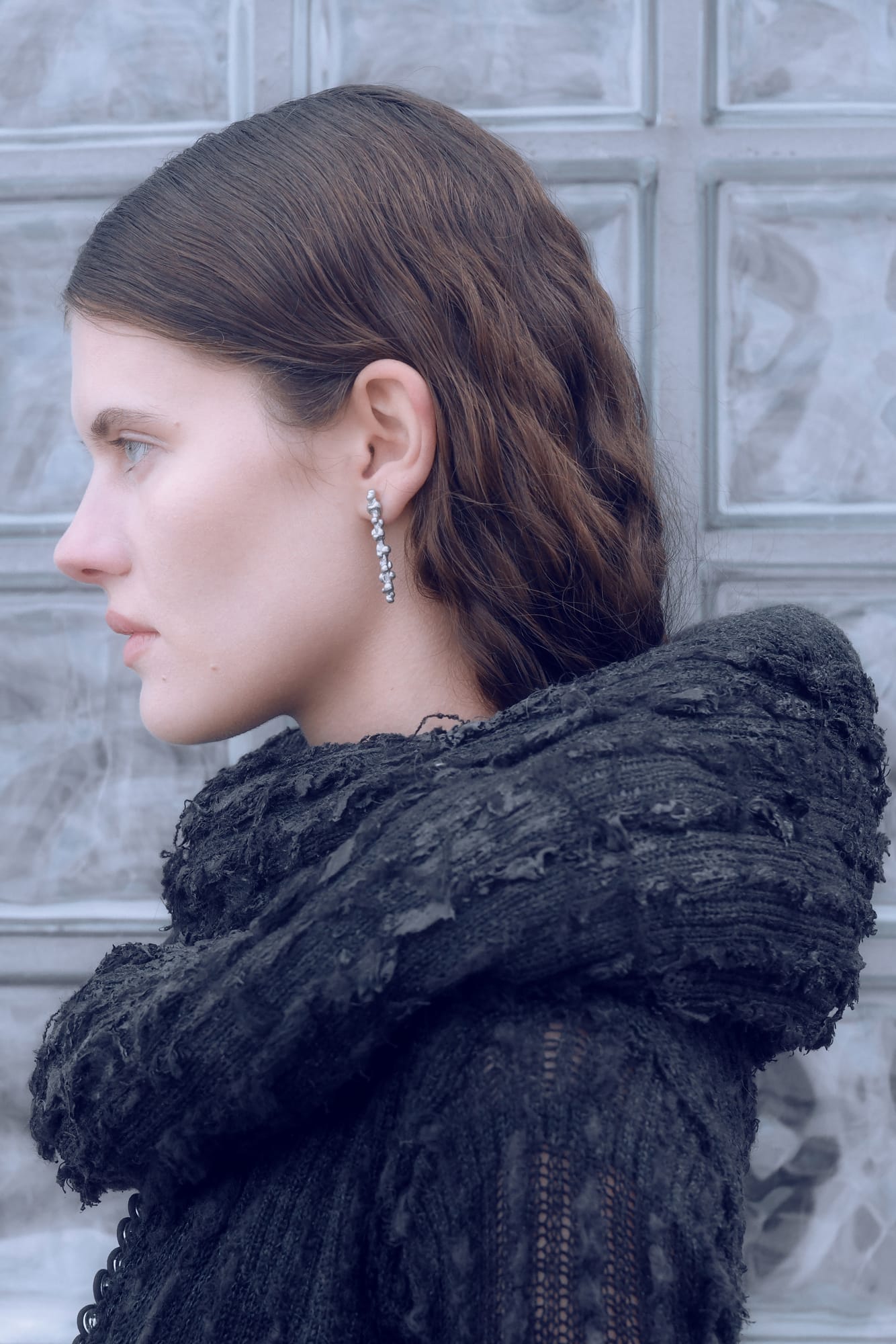 profile of a person with wavy hair wearing a long silver earring