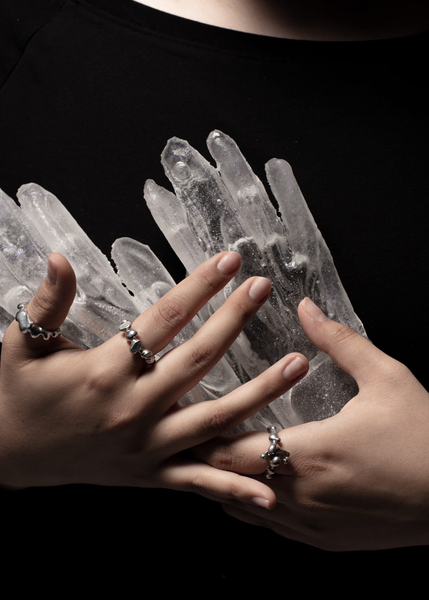 hands wearing silver rings holding a cluster of clear quartz