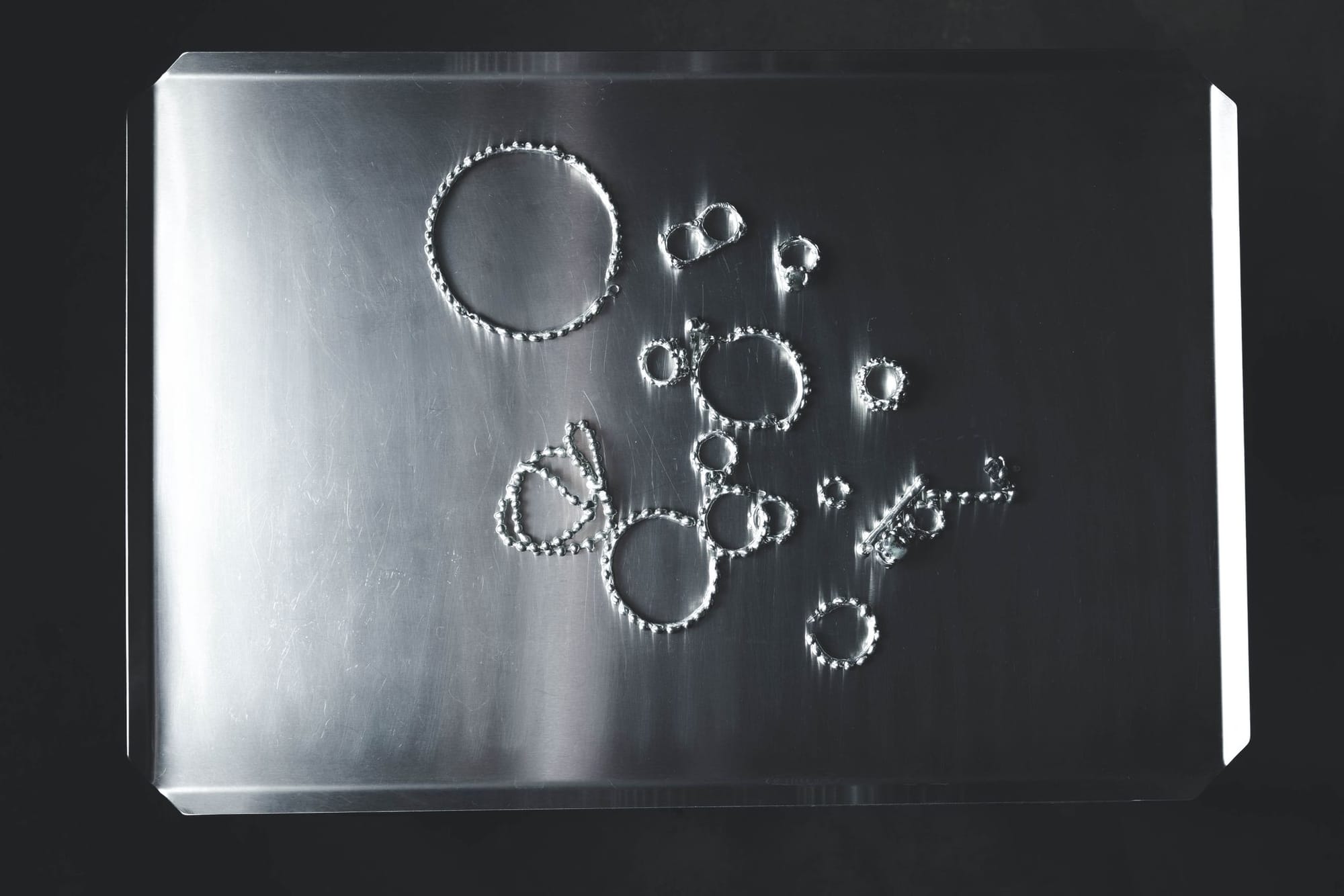 beaded silver rings and hoops scattered across a steel tray