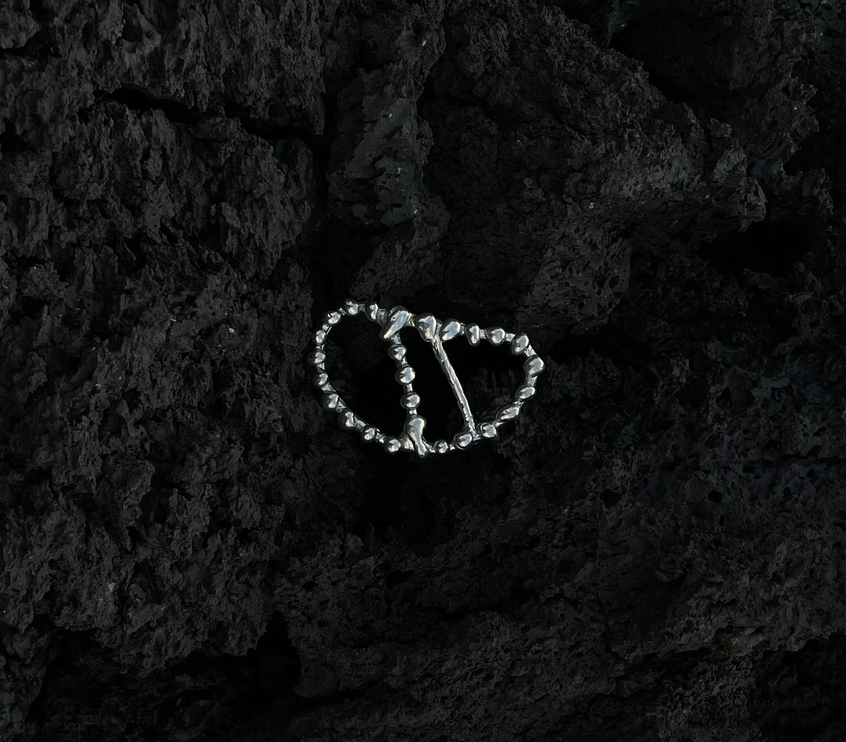 a beaded silver piece lying on black volcanic rock